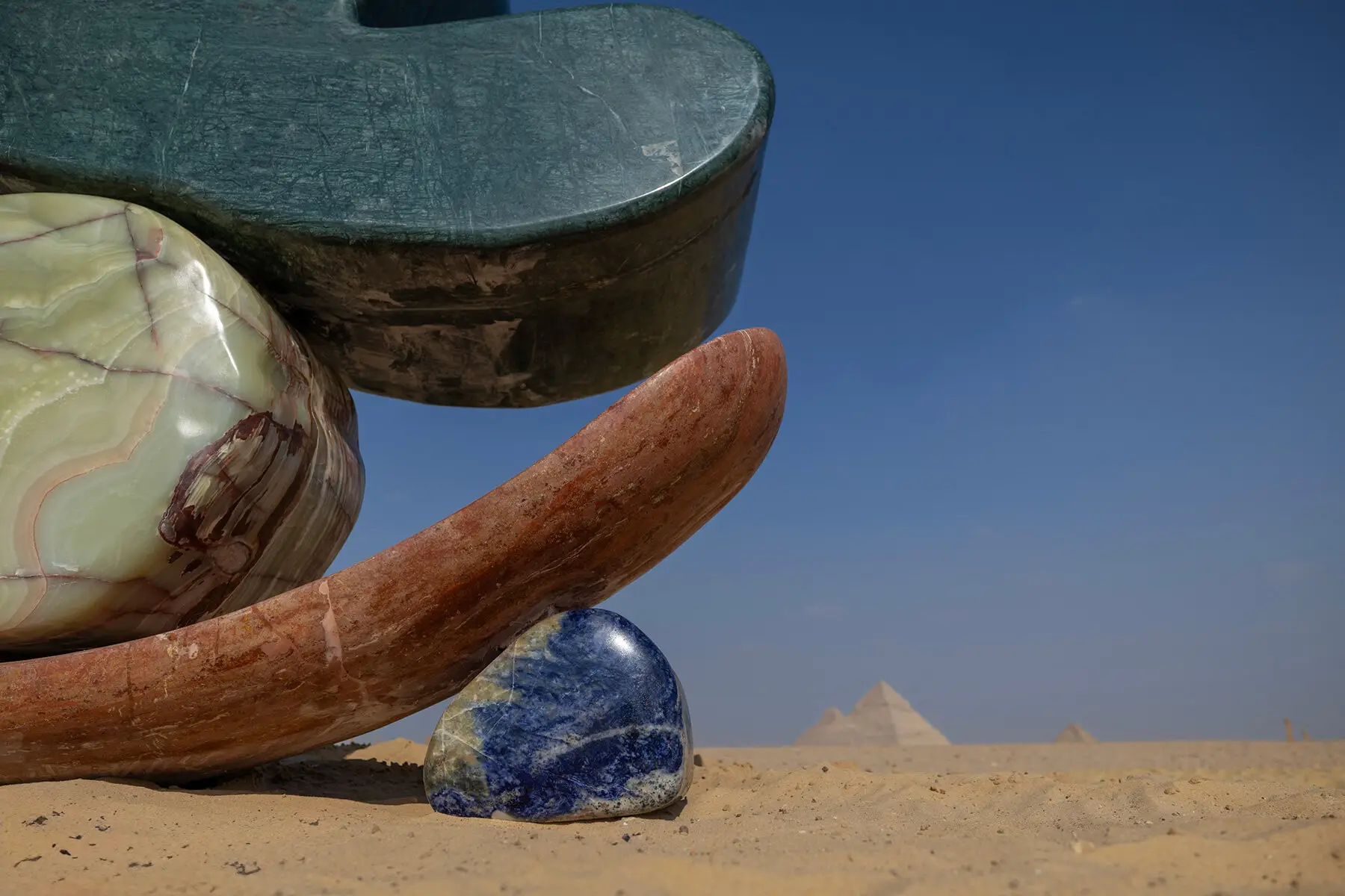 a reddish-brown lower curve grounds the piece in the sand
